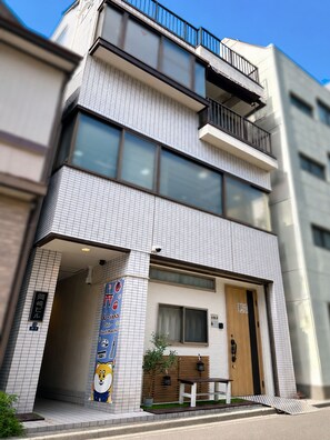 Un edificio moderno con fachada de azulejos, puerta de madera y un pequeño espacio exterior con mesas.