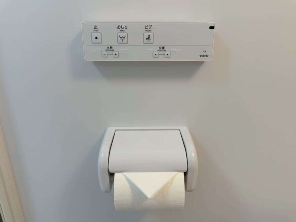 A white toilet paper holder with a roll of toilet paper on a plain wall.