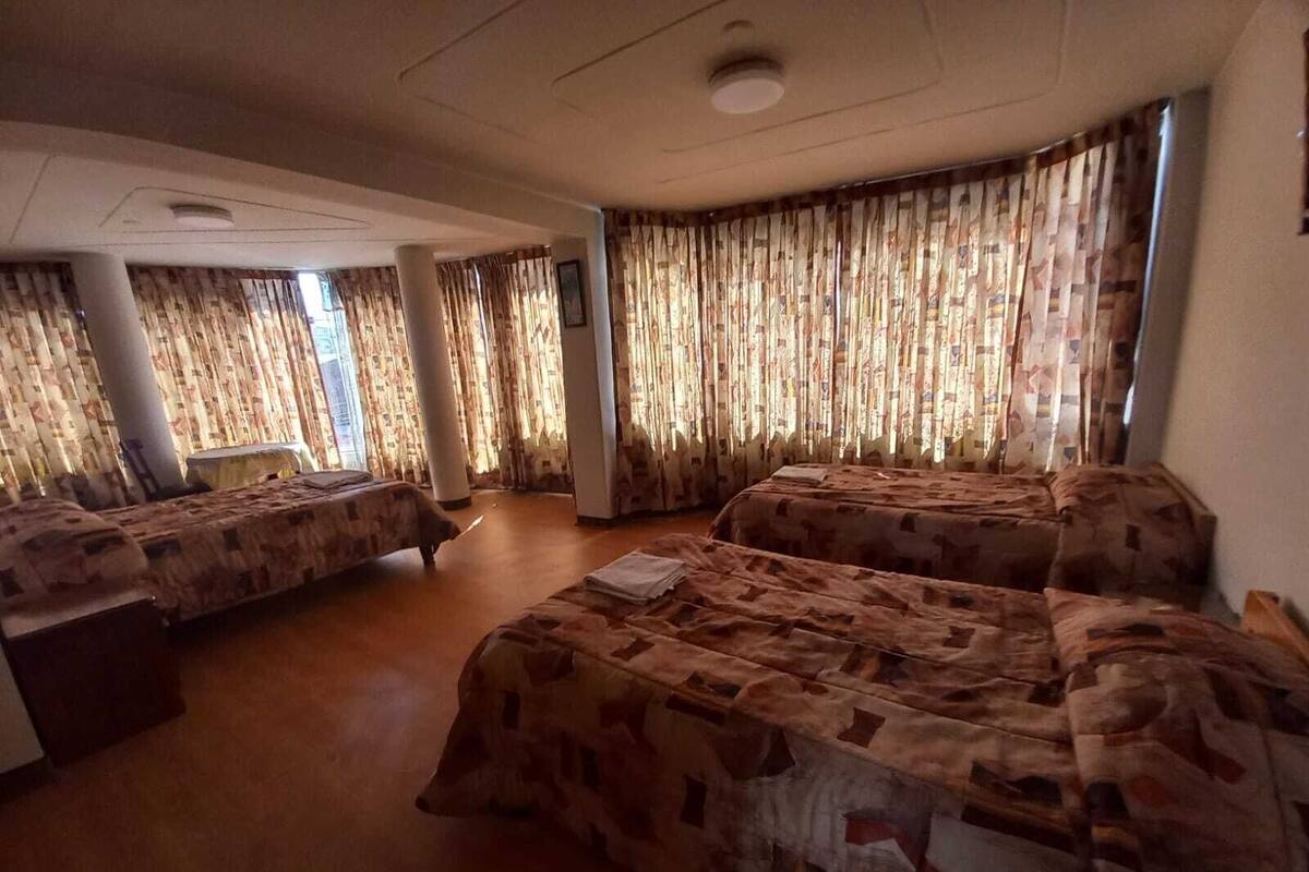A room with three beds, patterned curtains, and a wooden floor.
