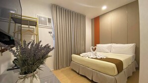 A modern hotel room with a bed, a potted plant, a mirror, and a window with curtains. - Iloilo Grand Hotel (Iloilo)