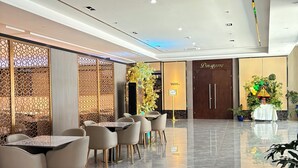 A modern hotel lobby with a marble floor, seating area with tables and chairs, decorative plants, and a reception desk. - Iloilo Grand Hotel (Iloilo)
