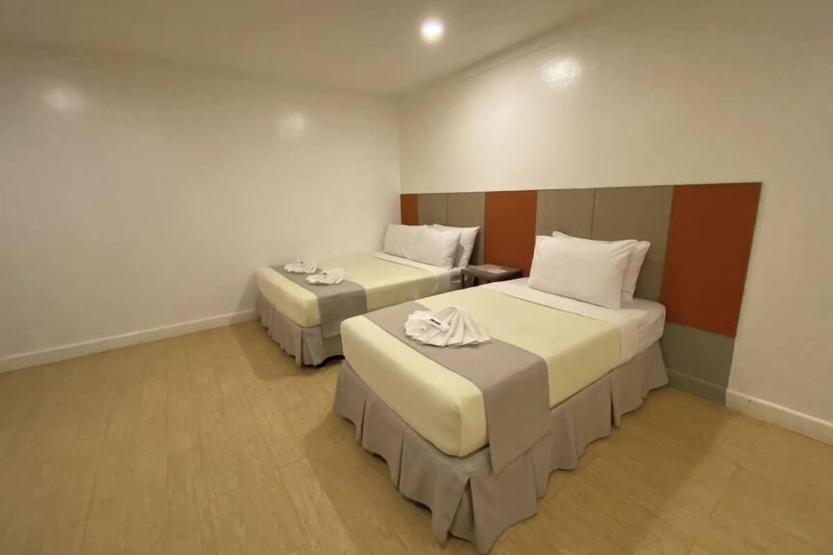 A hotel room with two beds, each with a grey bedspread and white pillows, and a wooden floor.