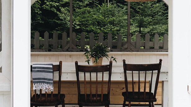 Een veranda met drie rieten hanglampen, houten stoelen en een potplant.