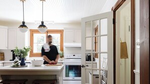 Een keuken met witte kastjes, een groot eiland met krukken, een fornuis en hangende hanglampen.