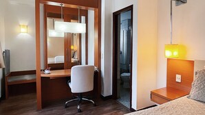 Habitación de hotel con cama, escritorio, silla, espejo y puerta de baño.