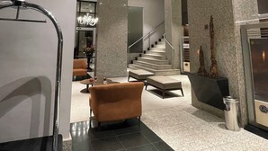 Un vestíbulo moderno con una escalera central, un área de descanso con sofá y sillones, y una mesa de recepción.