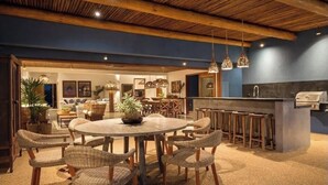 A spacious dining area with a round table and wicker chairs, a bar with stools, and a kitchen with a grill.
