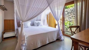 A bed with a canopy, a wooden bench, a table, and a view of greenery outside.
