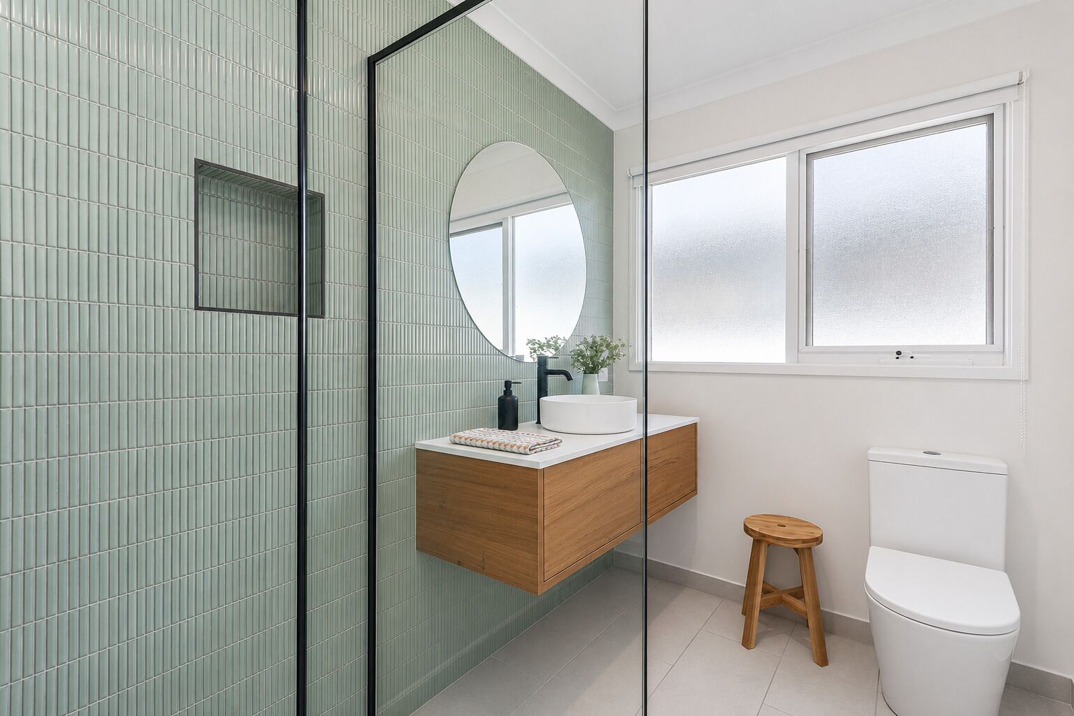 Une salle de bain moderne avec une douche à parois de verre, un meuble-lavabo en bois, un miroir rond et des toilettes.