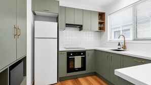 A modern kitchen with a built-in oven, a refrigerator, and a window with blinds.