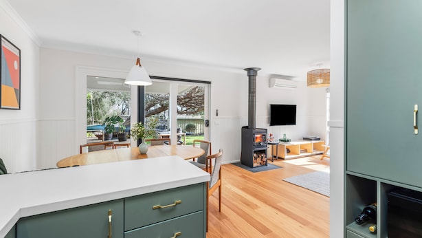 A modern kitchen with a white countertop, green cabinets, and a dining area with wooden furniture.