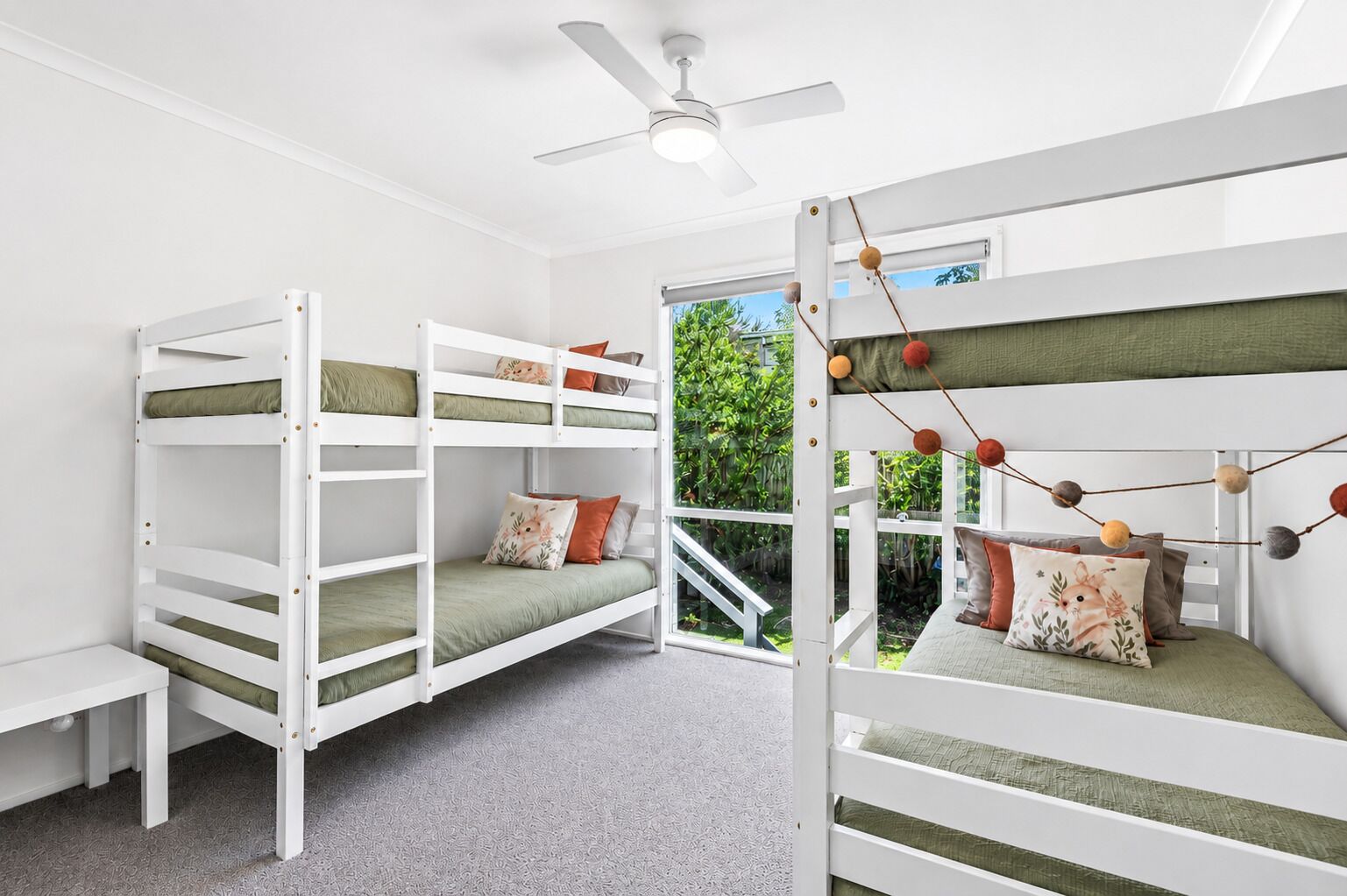 A room with bunk beds, a ceiling fan, and a view of greenery outside.