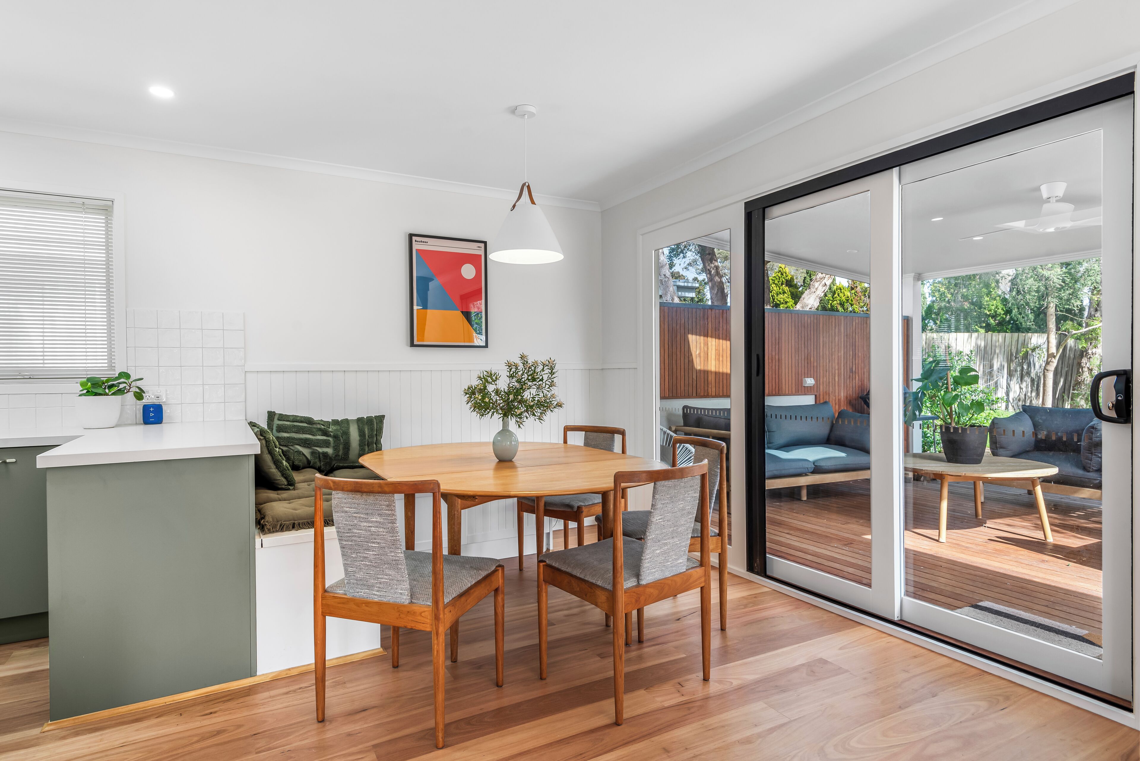 A modern kitchen with a dining area, a large window, and a sliding glass door leading to an outdoor seating area.