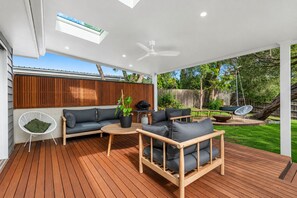 An outdoor patio with a wooden deck, a sofa, a coffee table, and a hanging chair.