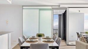 A modern dining area with a large table set for six, surrounded by chairs, and a view of the city through large glass doors. - Circle on Cavill River View (Surfers Paradise)