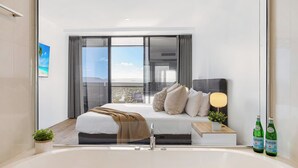 A modern bedroom with a large bed, a bedside table with a lamp, and two bottles of Pellegrino water. - Circle on Cavill River View (Surfers Paradise)