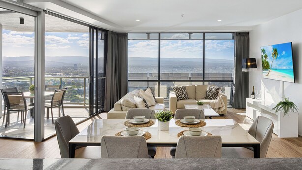 A modern living room with a large dining table, comfortable seating, and a city view through expansive windows. - Circle on Cavill River View (Surfers Paradise)