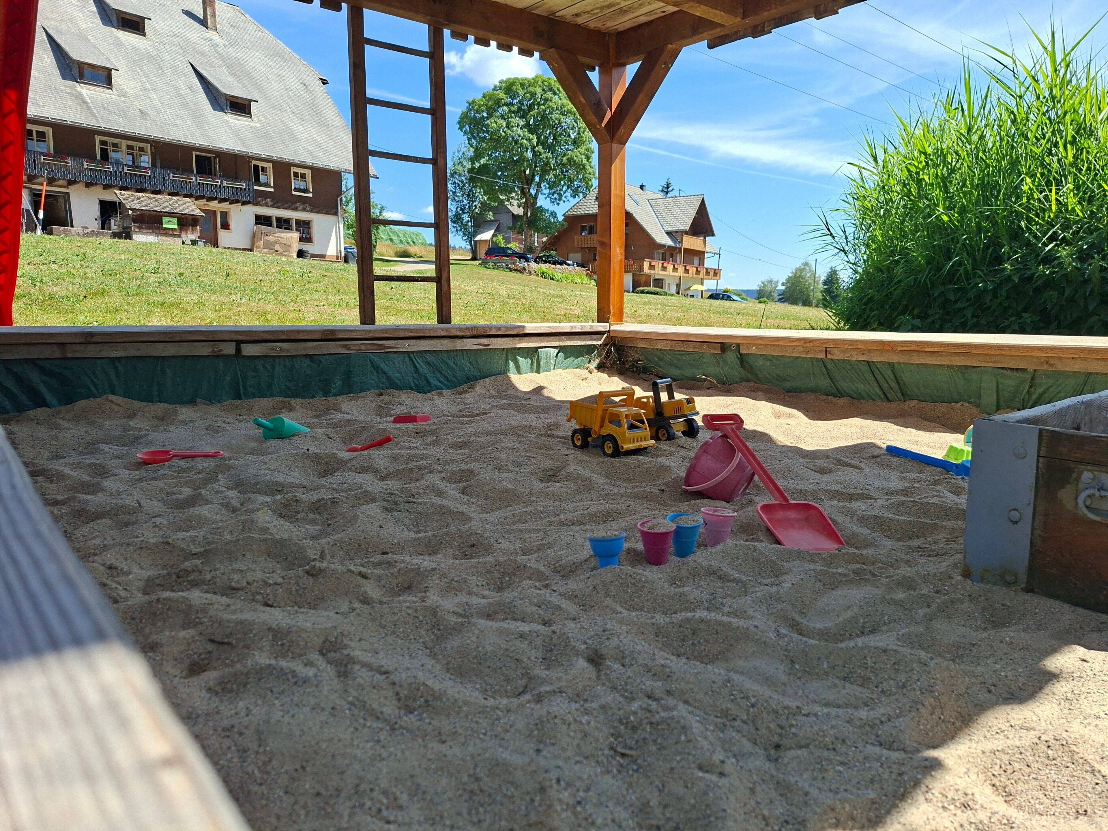 Ein Sandspielbereich mit Spielzeug und einer Holzkonstruktion.