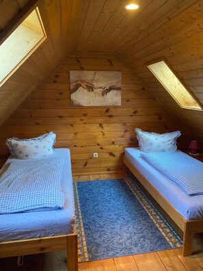 A small, cozy attic bedroom with wooden walls and sloped ceilings, featuring two single beds with matching pillows and a blue rug. - Holiday Apartment 'Mühlenblick' with Shared Terrace, Garden, Farm Stay Experience (Eisenbach)