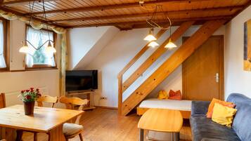 Une pièce confortable de style loft, avec un plafond en bois, une table à manger avec des chaises, un canapé avec des coussins, un téléviseur et un escalier.