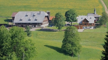En lantlig miljö med en stor byggnad som ser ut att vara ett hotell, omgiven av öppna fält och träd.