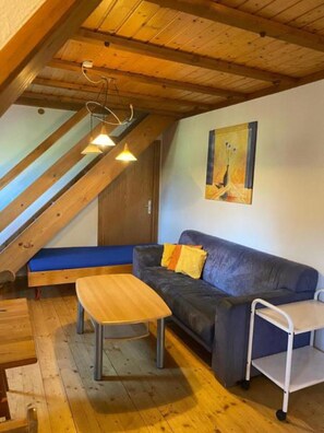 A cozy room with a wooden ceiling, a blue sofa, a wooden table, and a painting on the wall. - Holiday Apartment 'Mühlenblick' with Shared Terrace, Garden, Farm Stay Experience (Eisenbach)