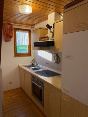 A compact kitchen with wooden cabinets, a built-in oven, a sink, and a window with a view of greenery.