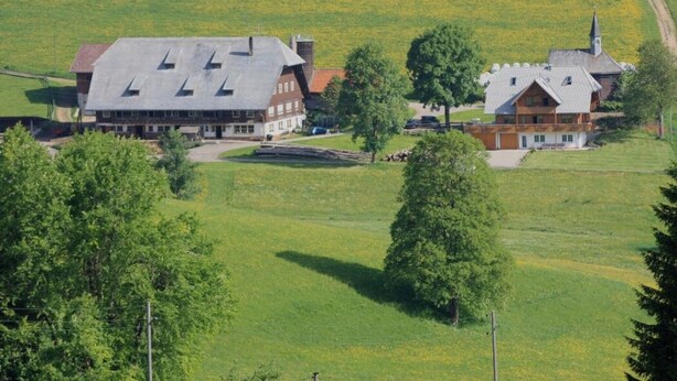 Ländliche Umgebung mit einem großen Gebäude, das wie ein Hotel wirkt, umgeben von Feldern und Bäumen.