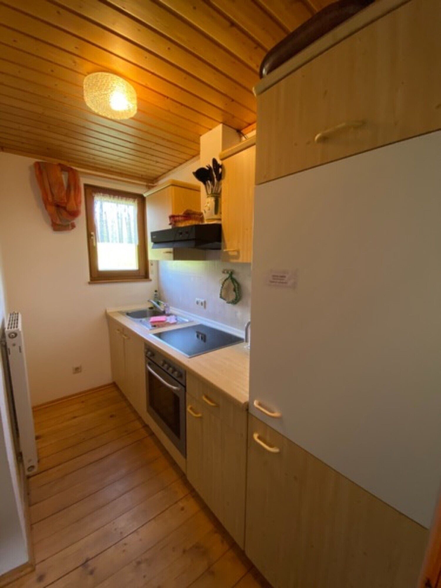 Ett kompakt kök med träskåp, en inbyggd ugn, ett handfat och ett fönster med gardiner.