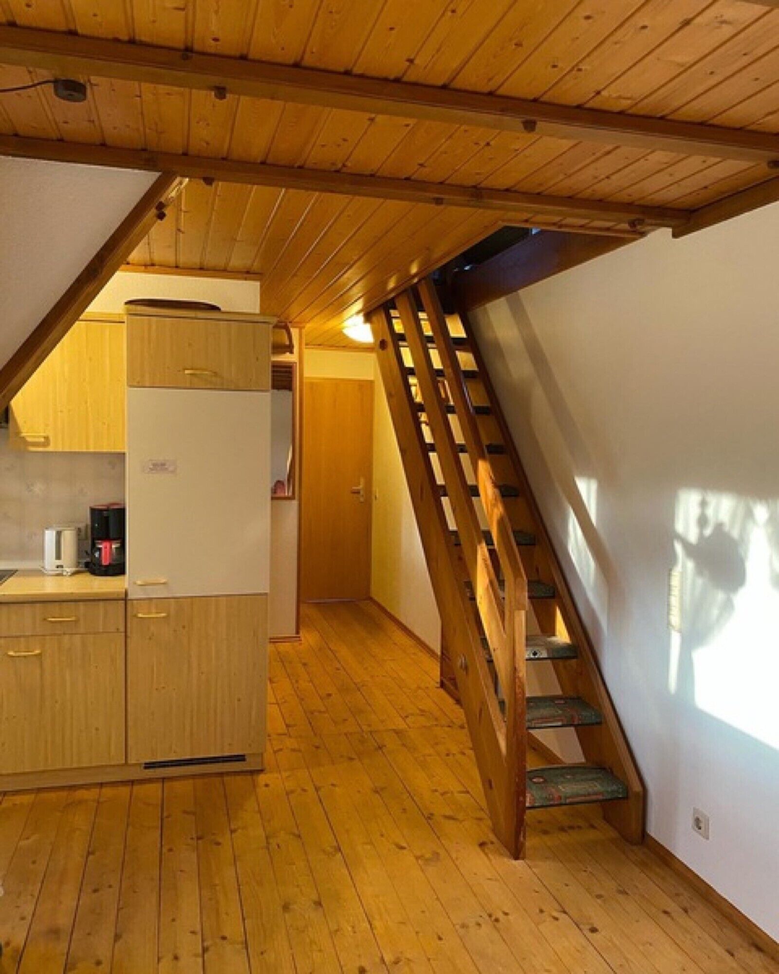 A wooden interior with a kitchen, a staircase, and a door leading to another room.