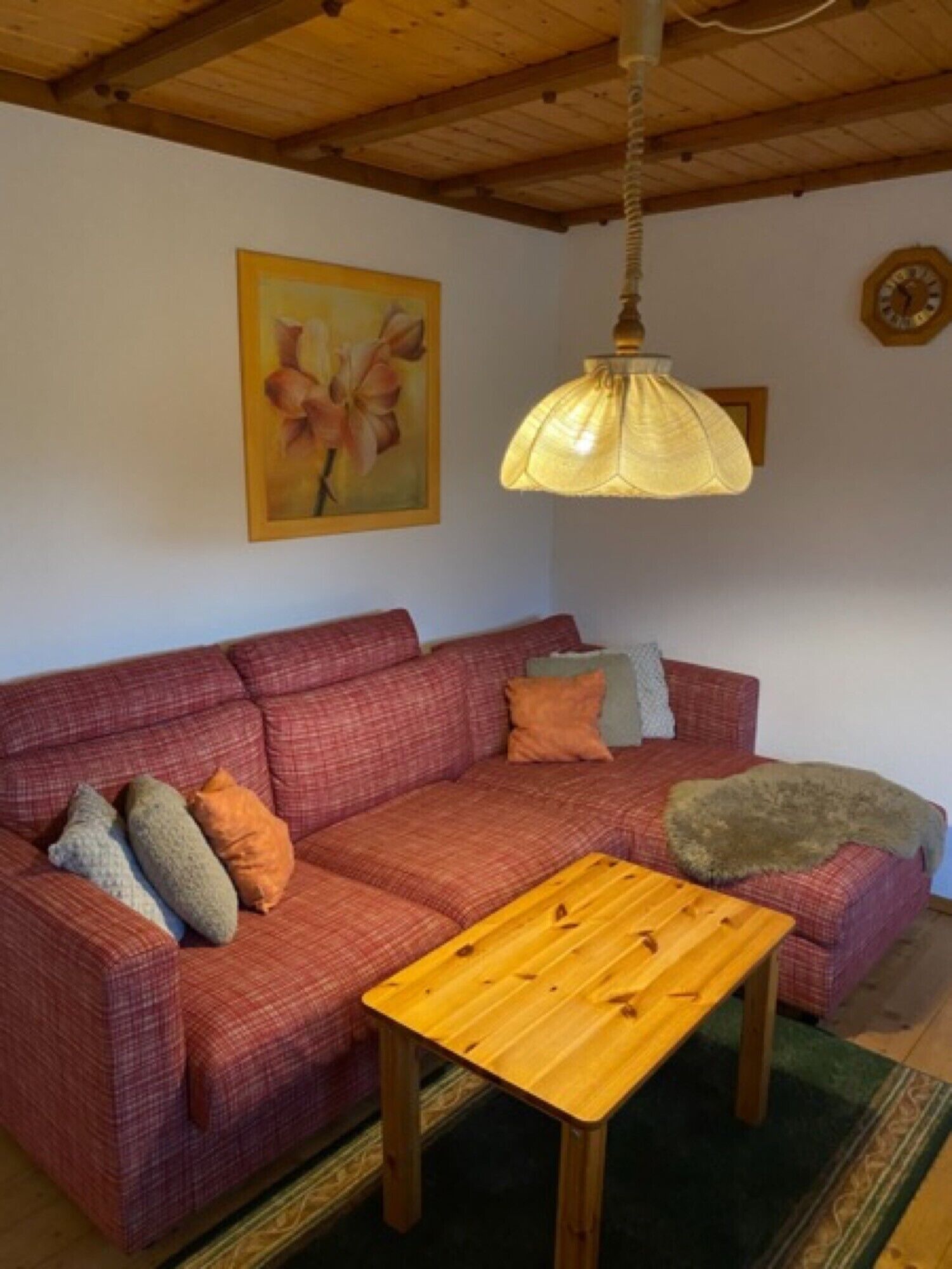 Ein gemütliches Wohnzimmer mit einem roten Sofa, einem Holztisch, einer Hängelampe und einem Bild an der Wand.