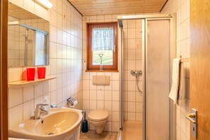 Et badeværelse med vask, toilet, bruser og et vindue med udsigt til en have.