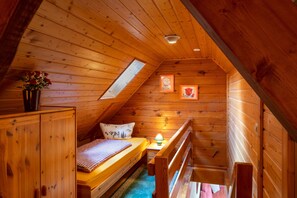 A cozy attic bedroom with a wooden sloped ceiling, a single bed with a checkered bedspread, a nightstand with a lamp, and a window with a view of the sky. - Apartment 'Obertalblick' on a Farm Holiday (Eisenbach)