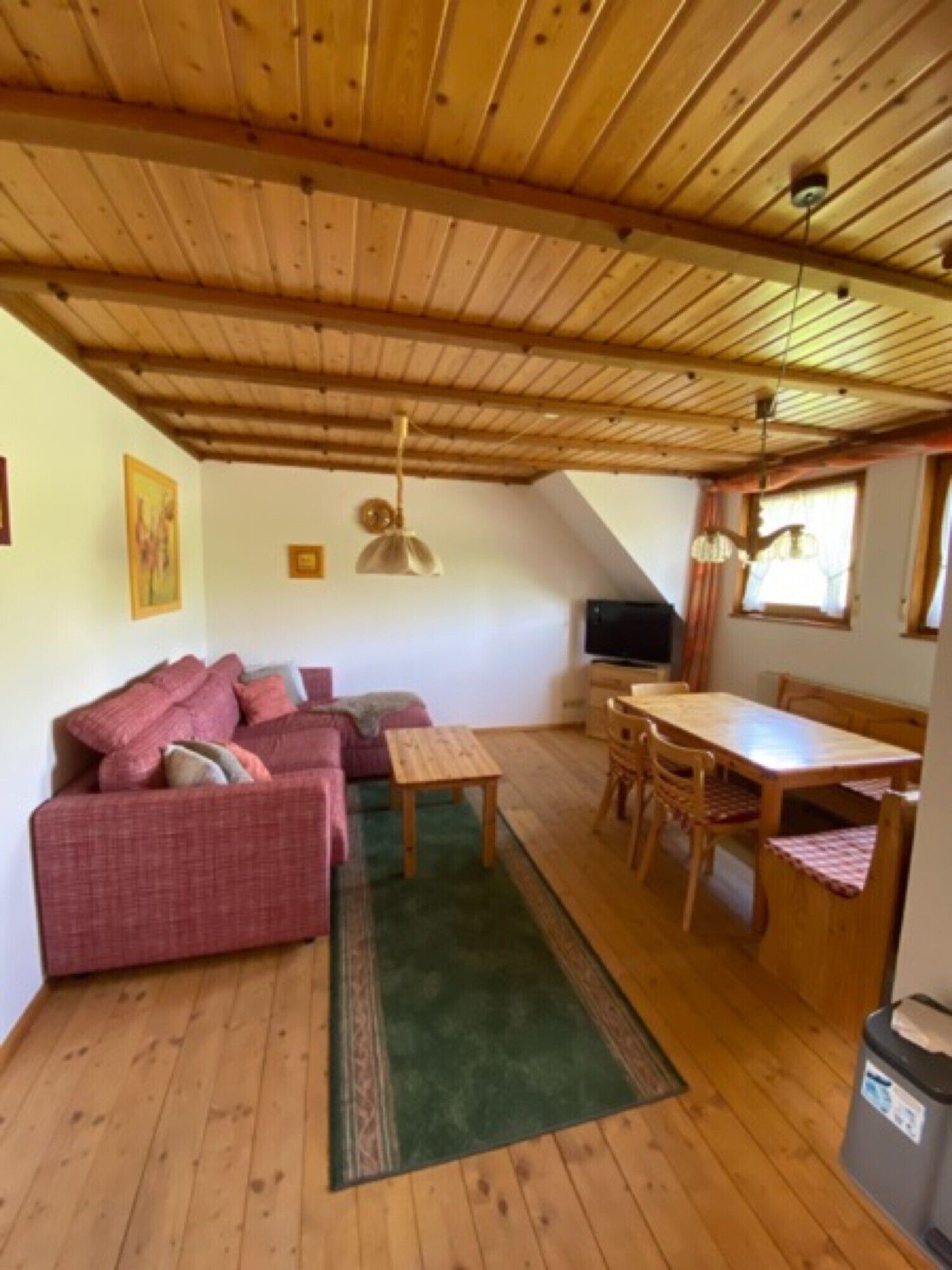 A cozy room with a wooden ceiling, a sofa, a dining table with chairs, and a small rug.