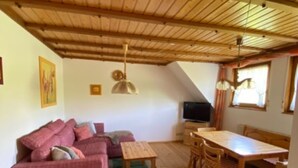 Ein gemütliches Zimmer mit Holzbalkendecke, einer Couch, einem Esstisch mit Stühlen und einem kleinen Teppich.