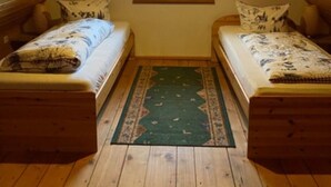 Ein kleines Schlafzimmer unter dem Dach mit zwei Holzbettchen, einem Fenster mit Blick und einem grünen Teppich.