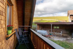 A balcony with a view of a farm, a wooden building, and a fenced area with farm equipment. - Apartment 'Obertalblick' on a Farm Holiday (Eisenbach)