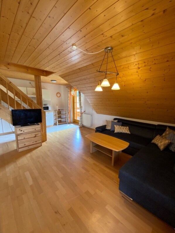 A wooden interior with a staircase, a TV on a wooden cabinet, a sofa, and a coffee table.