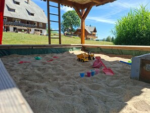 Un espace de jeux sablonneux avec des jouets et une structure en bois.
