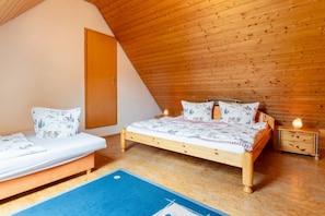 Une chambre avec un plafond en pente, un lit en bois, deux tables de chevet et une petite table de nuit avec une lampe.