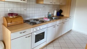 A kitchen with white cabinets, a wooden countertop, a stove, and a tiled backsplash. - Holiday Apartment 'Untertalblick' with Shared Garden and Balcony, Farm Stay (Eisenbach)