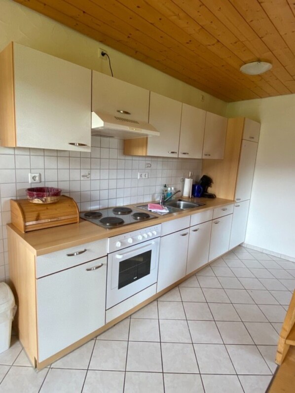 A kitchen with white cabinets, a wooden countertop, a stove, and a tiled backsplash. - Holiday Apartment 'Untertalblick' with Shared Garden and Balcony, Farm Stay (Eisenbach)