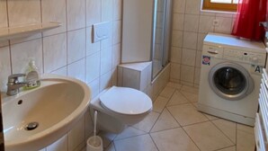 A compact bathroom with a sink, toilet, shower, and washing machine. - Holiday Apartment 'Untertalblick' with Shared Garden and Balcony, Farm Stay (Eisenbach)