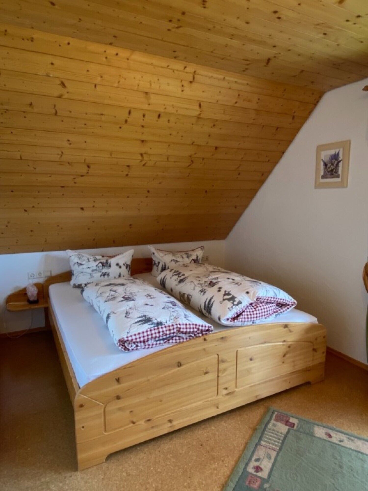 Ein Holzbett mit zwei Hängematten, einer karierten Decke und einem gerahmten Bild an der Wand.