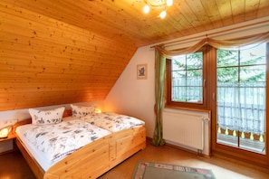 Quarto com teto de madeira, cama com roupa de cama estampada, janela com cortinas e radiador.