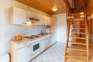 Cozinha moderna com armários brancos, bancada de madeira, fogão e forno embutido. Uma escada de madeira apoiada na parede.