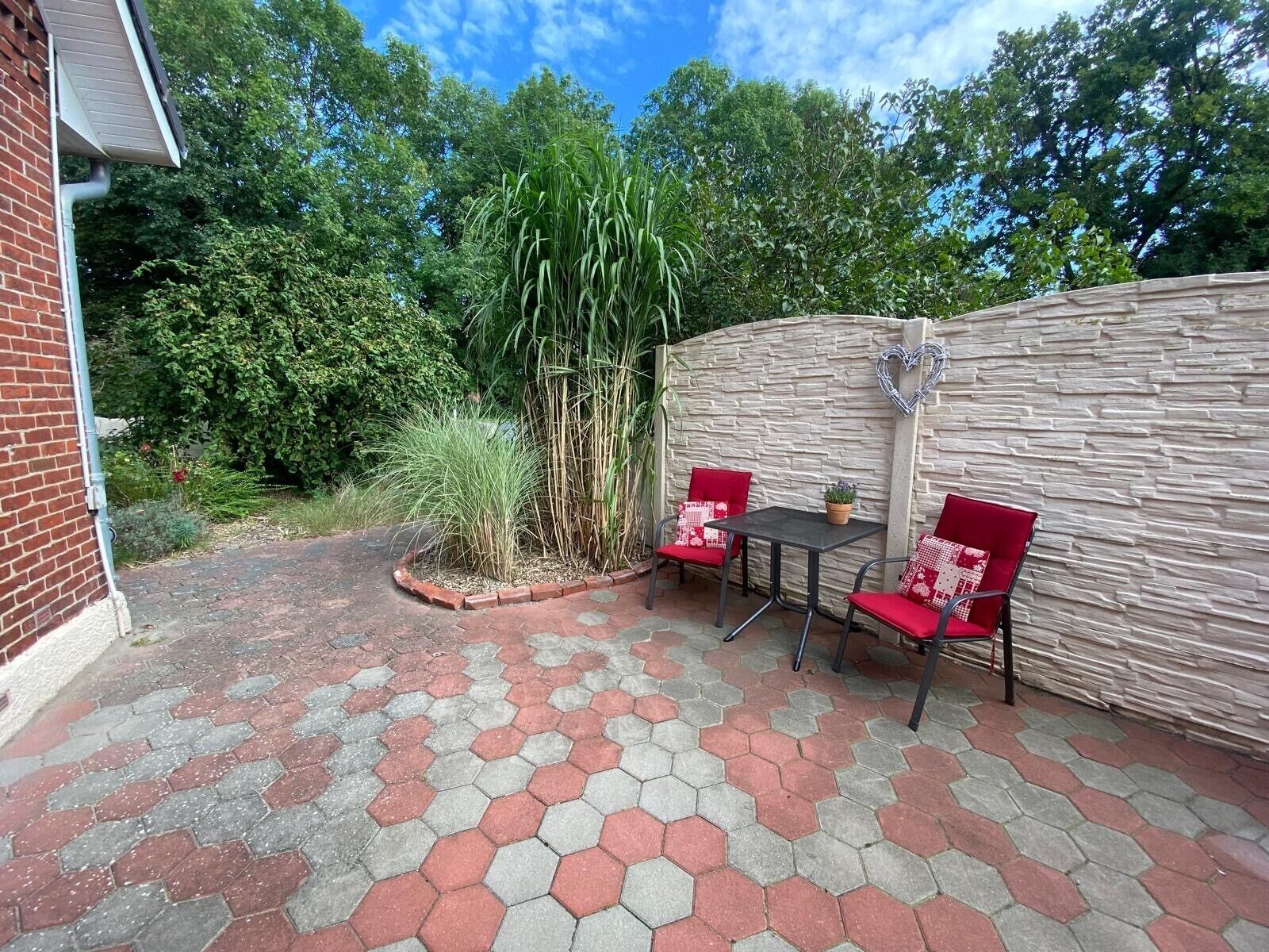 A patio with hexagonal tiles, two red chairs, a table, and a stone wall.