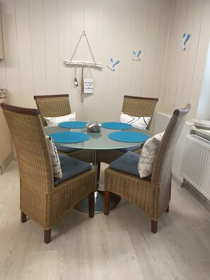 A dining area with wicker chairs, a glass table, and a wall-mounted light fixture.