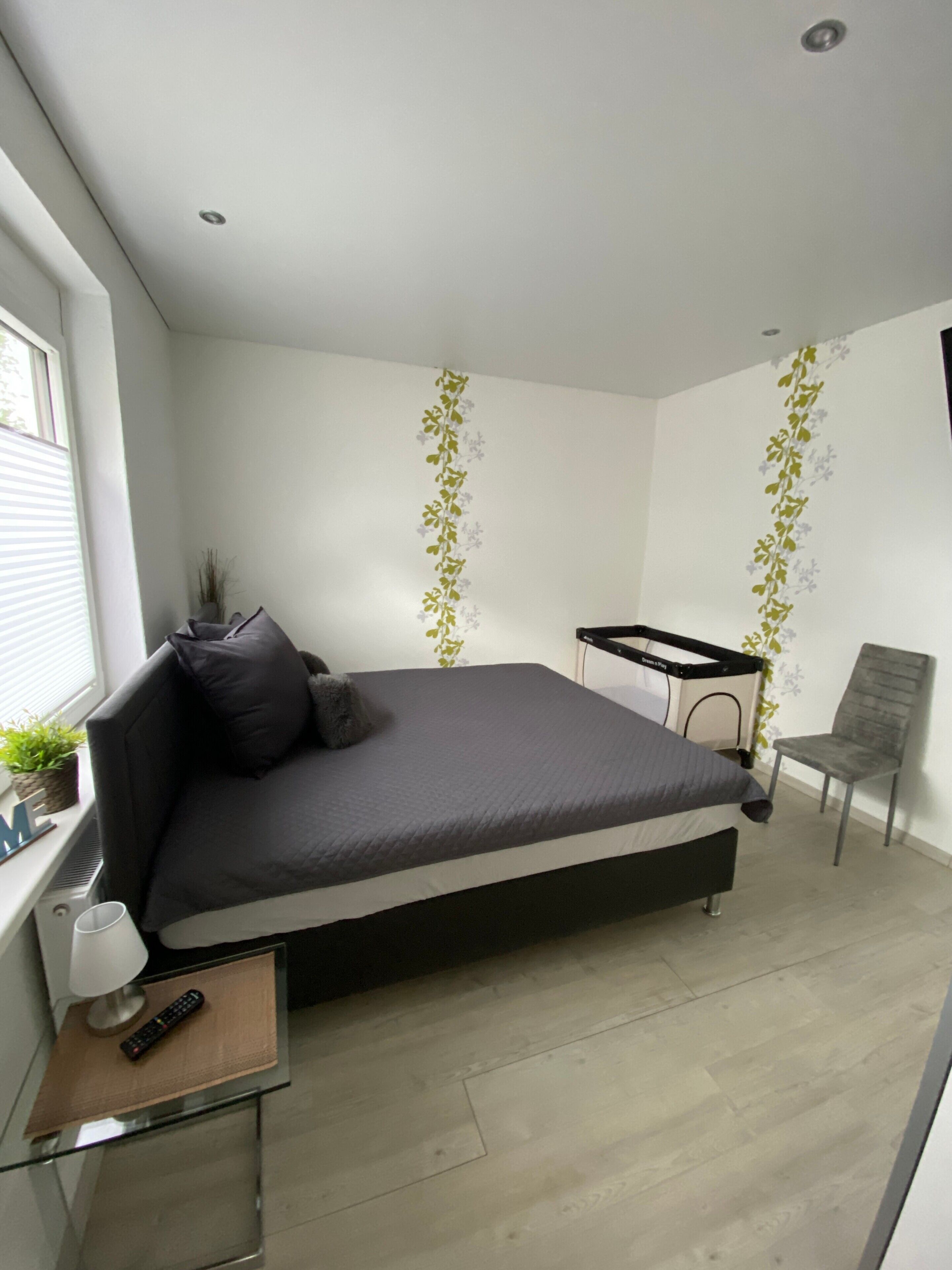 A bedroom with a bed, a desk, a chair, a window, and a plant.