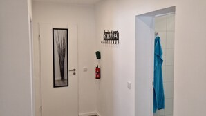 Un pasillo con piso de madera, una puerta blanca, un cuadro enmarcado, un extintor de incendios montado en la pared y una toalla colgada en la pared.